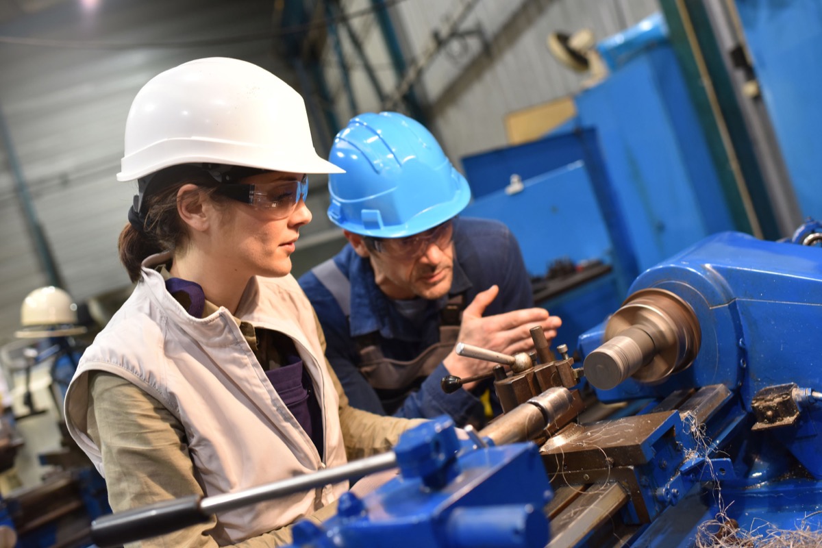 Metal worker teaching trainee on machine use; representing why unions must protect workers form automation