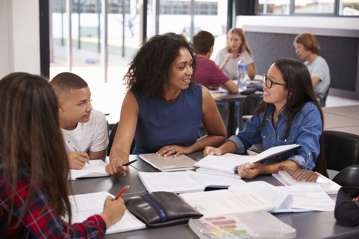 Teacher studying school books in class with high school kids; diverse and inclusive workplaces concept