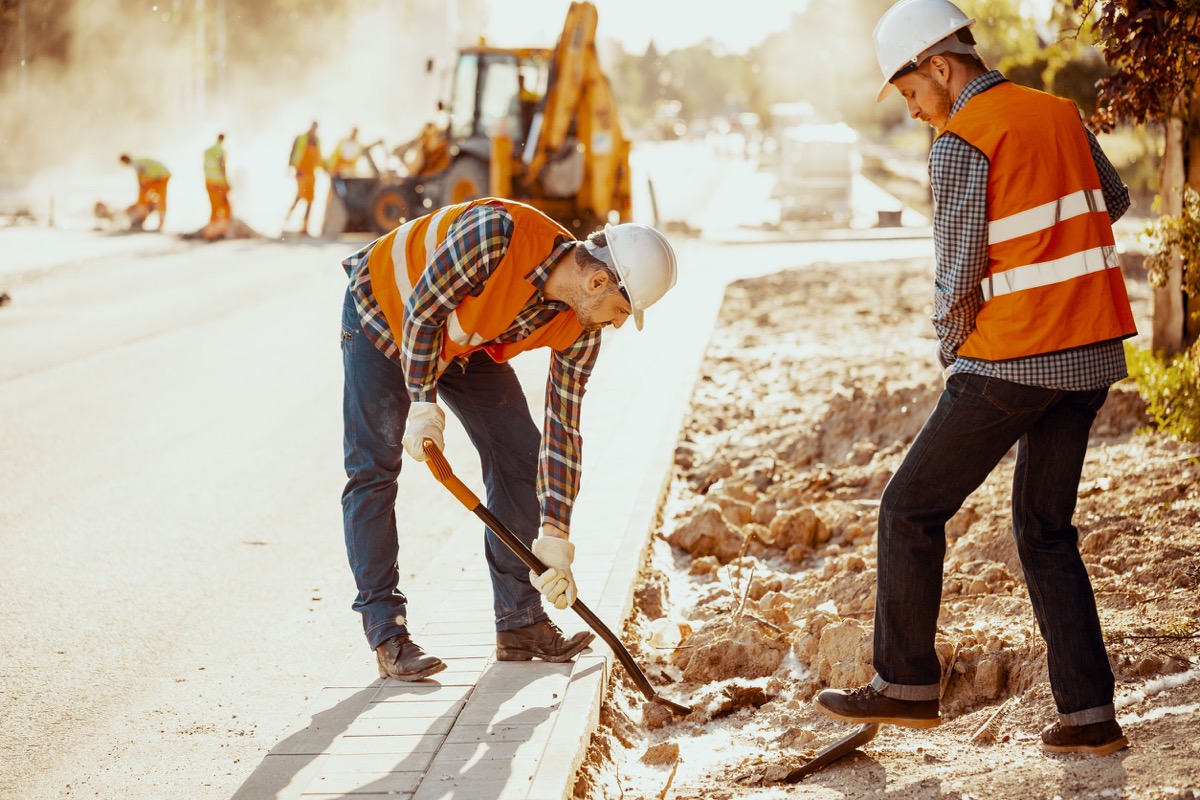 Workers in reflective vests using shovels during carriageway work; diverse and inclusive workplaces concept