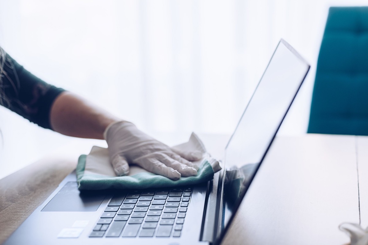Woman disinfects the laptop keyboard with spray disinfectant liquid; pandemic safety