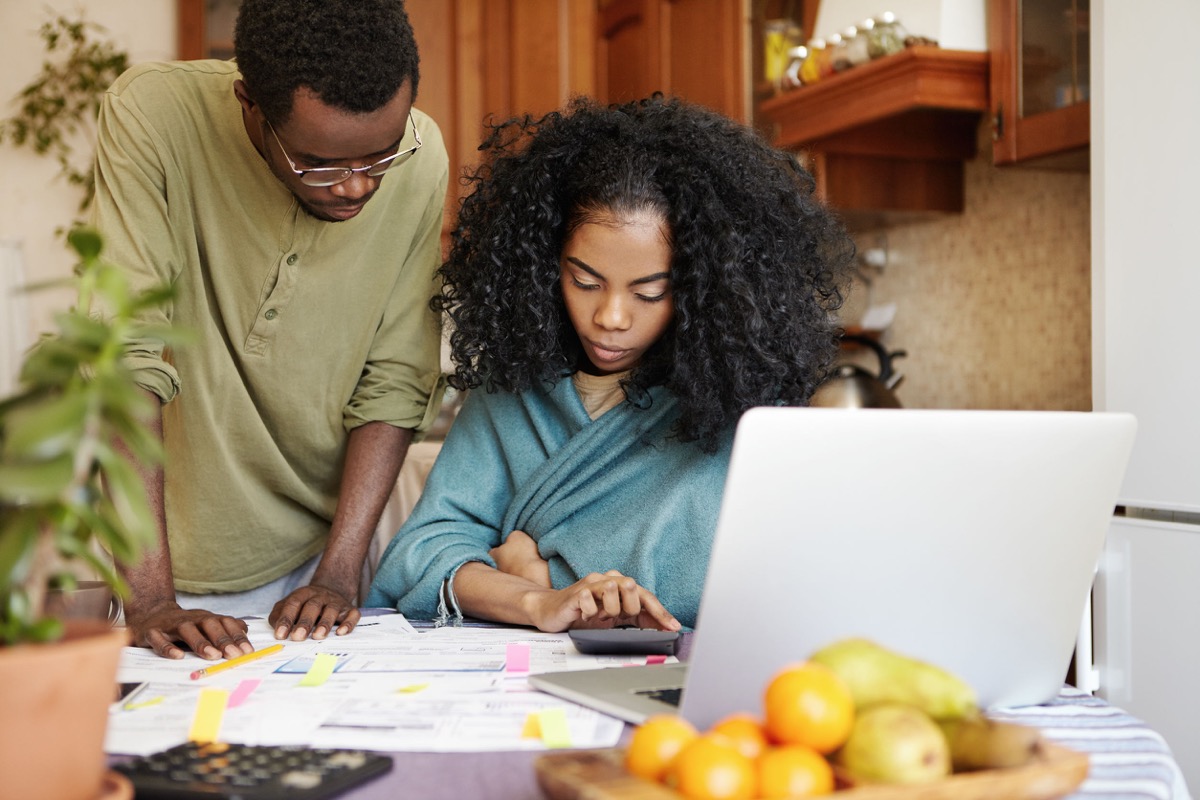 Serious wife and husband doing accounts and managing domestic budget together in kitchen; furloughed workers concept