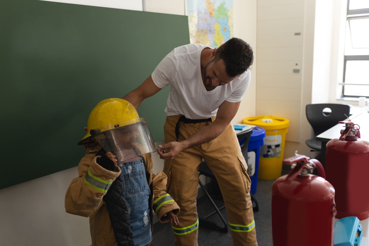 firefighter and schoolgirl in classroom of elementary school; iaff essential workers concept