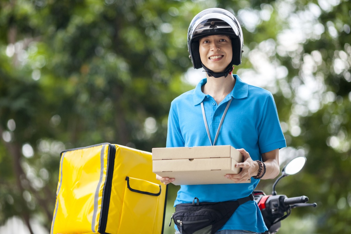 delivery driver holding pizzas smiles in front of their scooter; Organize Gig Workers concept