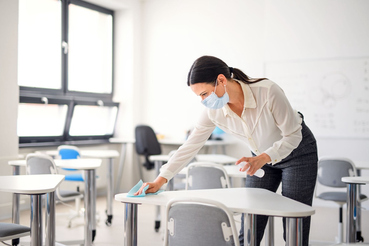 Teacher back at school after covid-19 quarantine and lockdown, disinfecting desks; teachers unions and reopening concept