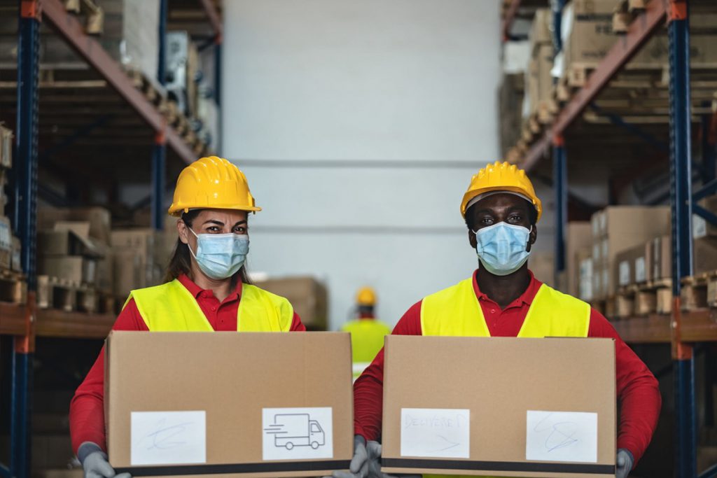 Team working in warehouse loading delivery boxes while wearing face surgical mask; ; supply shortages and union workers help in the pandemic concept