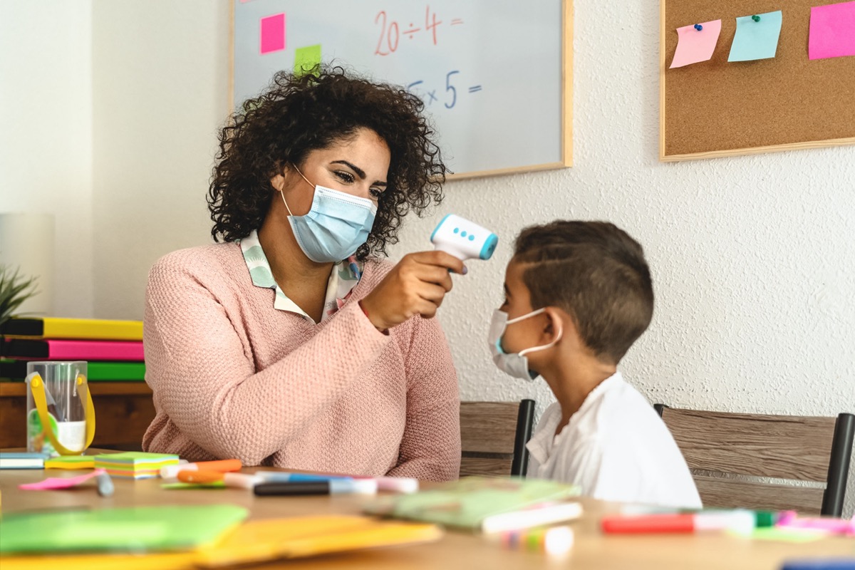 Teacher checks temperature on child in a classroom; teachers unions and reopening concept