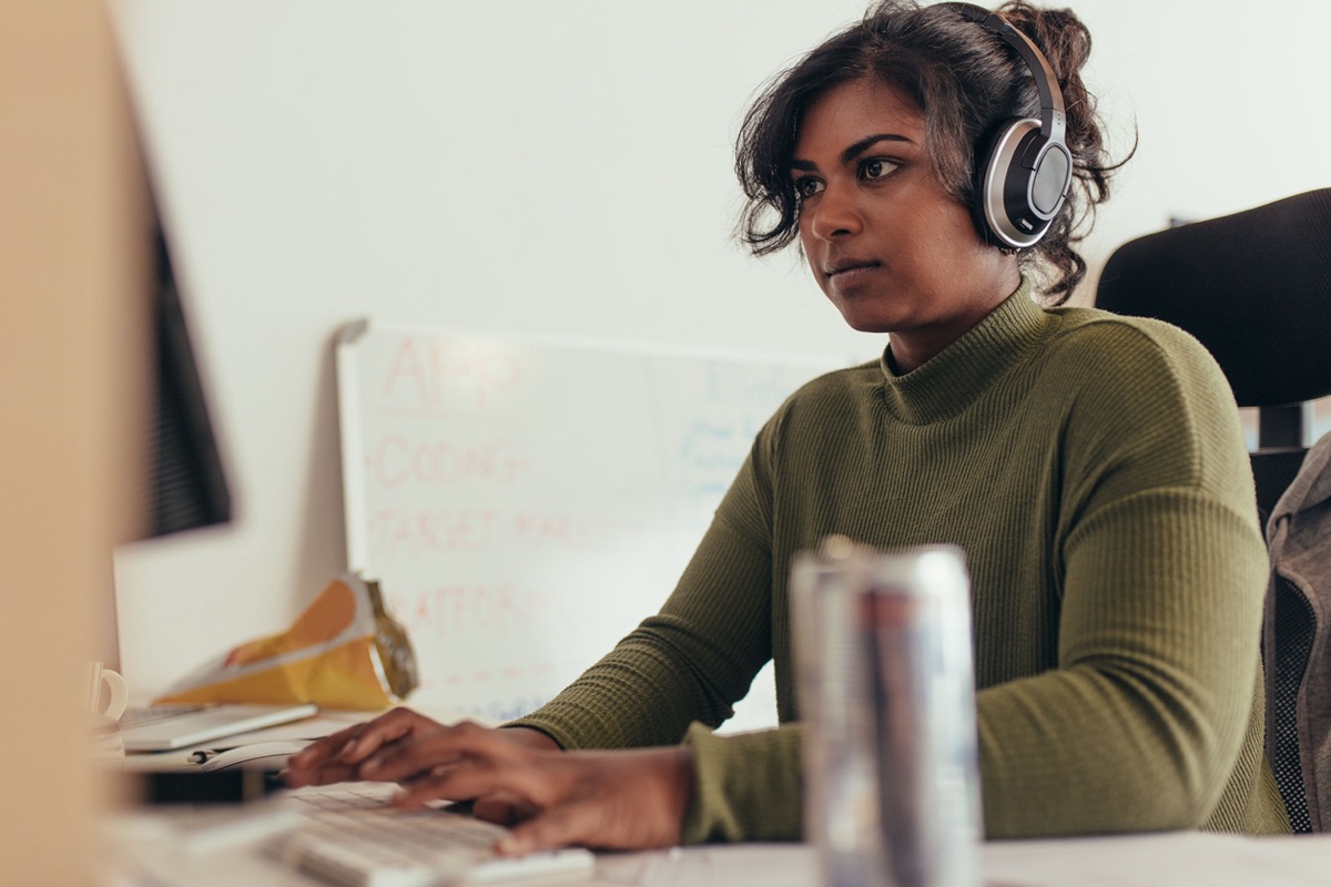 Woman wearing headphones coding on desktop computer; gig and tech workers need unions concept