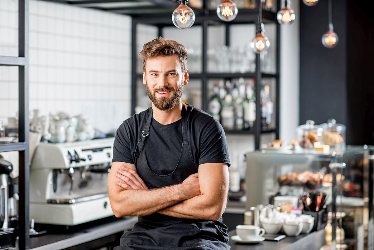 Portrait of a barista in black t-shirt and apron sitting at the bar of the modern cafe; union coffee shops concept