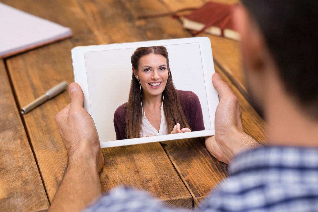 Closeup of a woman talking through video chat on tablet. Young man communicating with his girlfriend on tablet in video chat. Young man looking at screen of tablet and talking with a woman trought webcam.