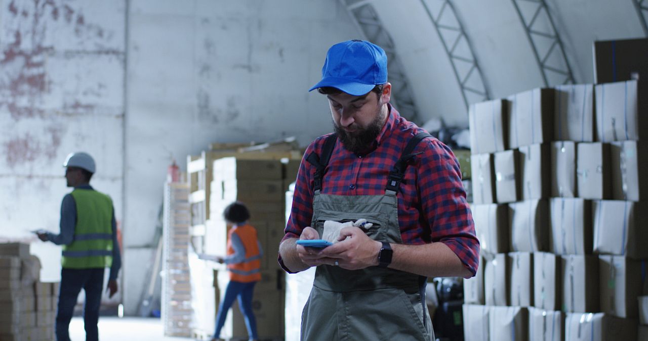 Medium shot of worker using phone in a warehouse; communication and digital tools concept