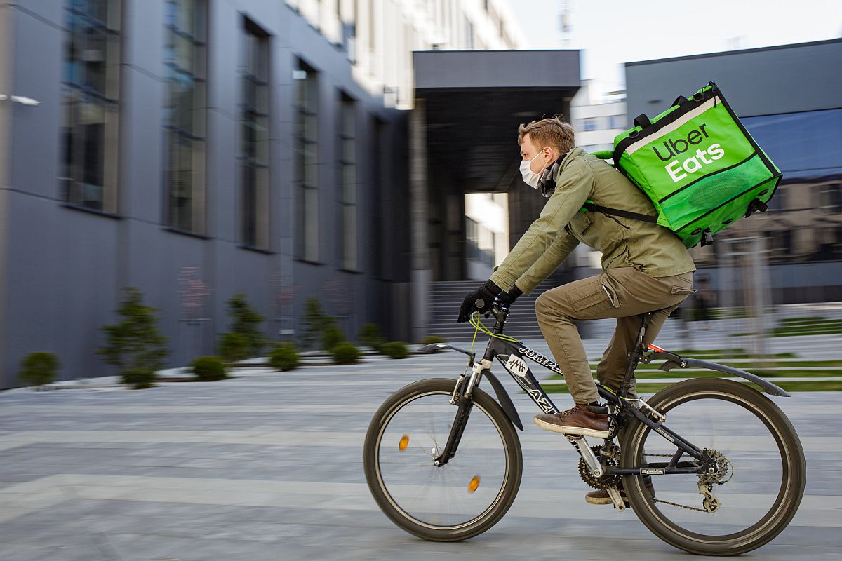 Food supplier with Uber Eats backpack riding a bike on the street; fight over Prop 22 concept