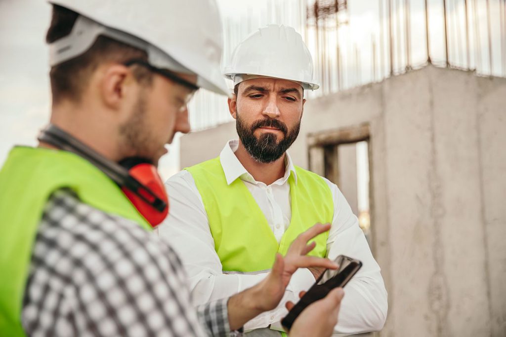 builders in protective hardhats using smartphone; ; digital union-busting concept