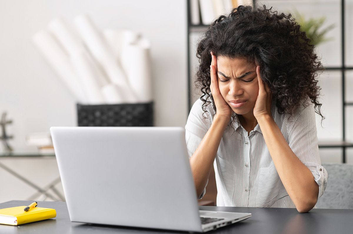 Young woman, frowning with head in hands, sits in front of her lap top; paid time off concept
