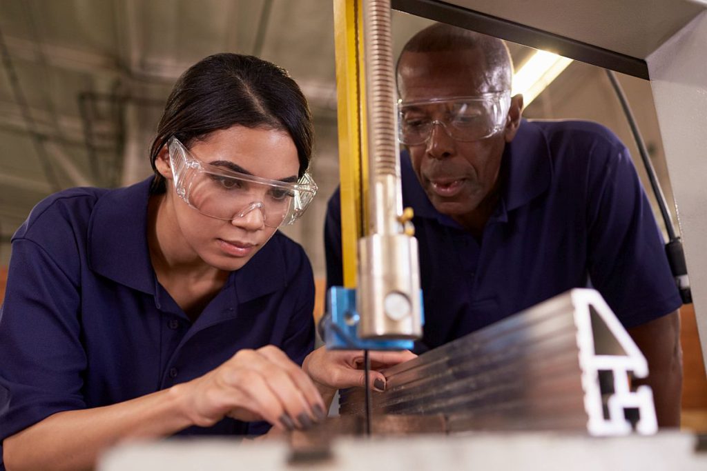 Young worker using tool, supervised by older worker; pro-worker initiatives concept