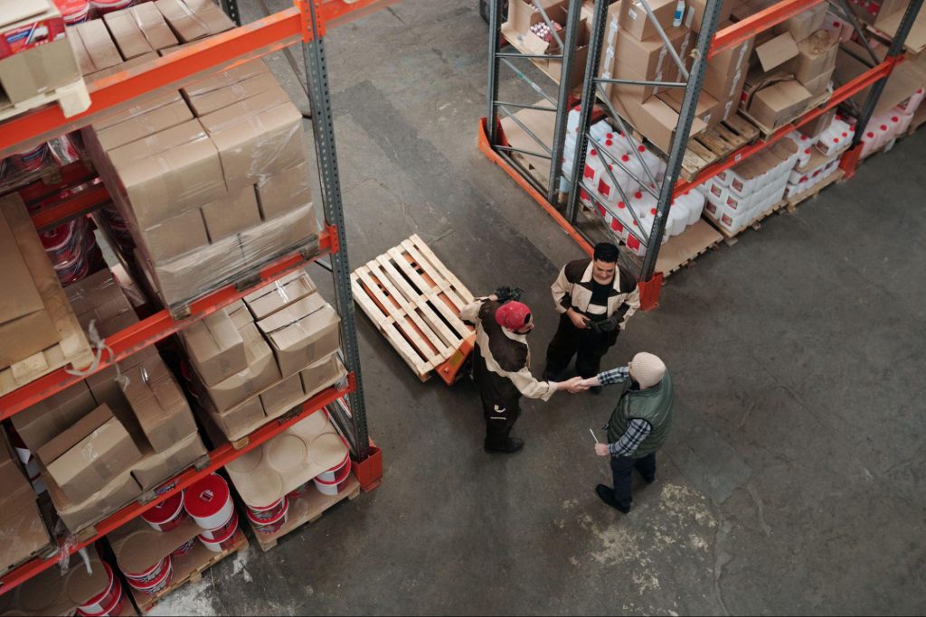 Three workers in warehouse, two shaking hands; new union concept