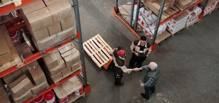 Three workers in warehouse, two shaking hands; new union concept