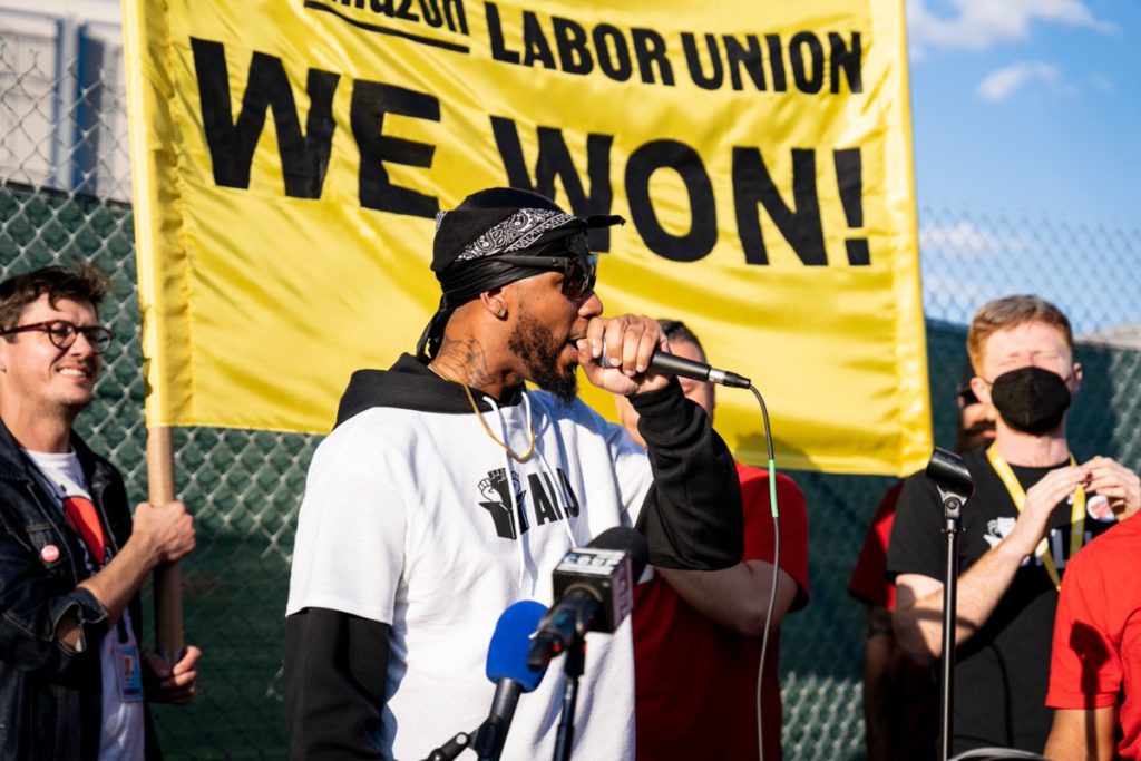 Union member speaking in front of a 'We Won!' sign; Amazon vs. ALU concept