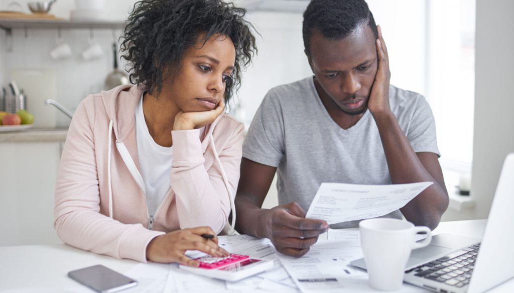 Couple looking at medical bills and using a calculator; healthcare benefits concept