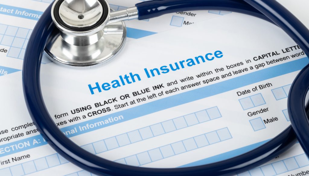 Health insurance paperwork with stethoscope lying on top; healthcare benefits concept